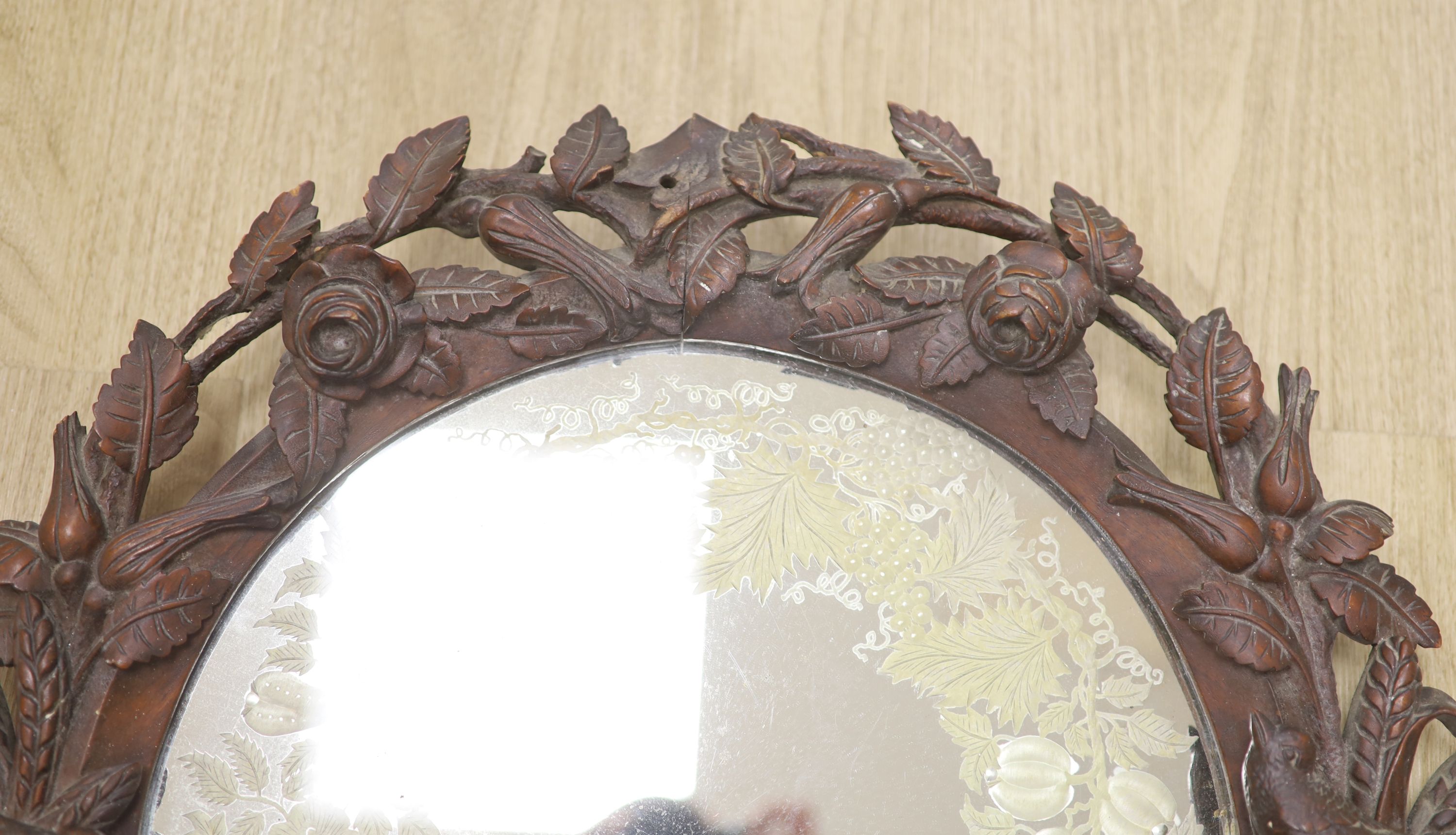 A Black Forest walnut wall mirror carved with roses, diameter 56cm